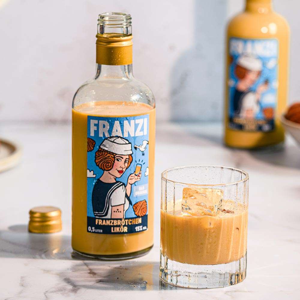 Eine geöffnete Flasche Franzi Franzbrötchenlikör neben einem Glas mit Franzbrötchenlikör 